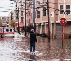 photo of a man standing in flood waters looking up at buildings with an ambulance in the background