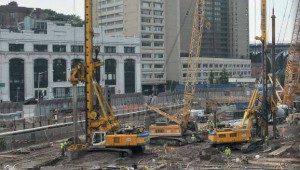 Photo of a construction site with 3 large, orange drilling rigs