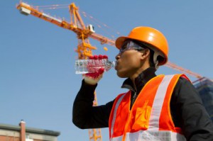 Engineer with safety vest and orange hat drinking water under construction crane